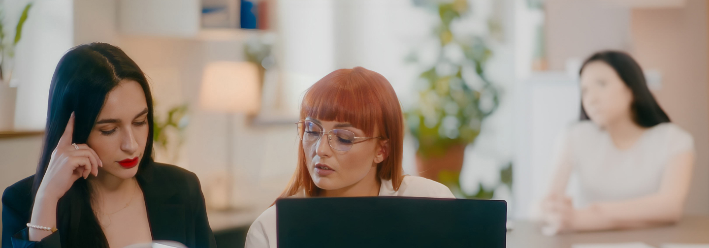 modern office setting, with two female colleagues collaborating on a laptop