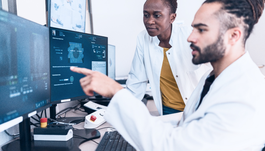 Two IT professionals reviewing real‑time analytics on large monitoring screens in Ergos operations center.