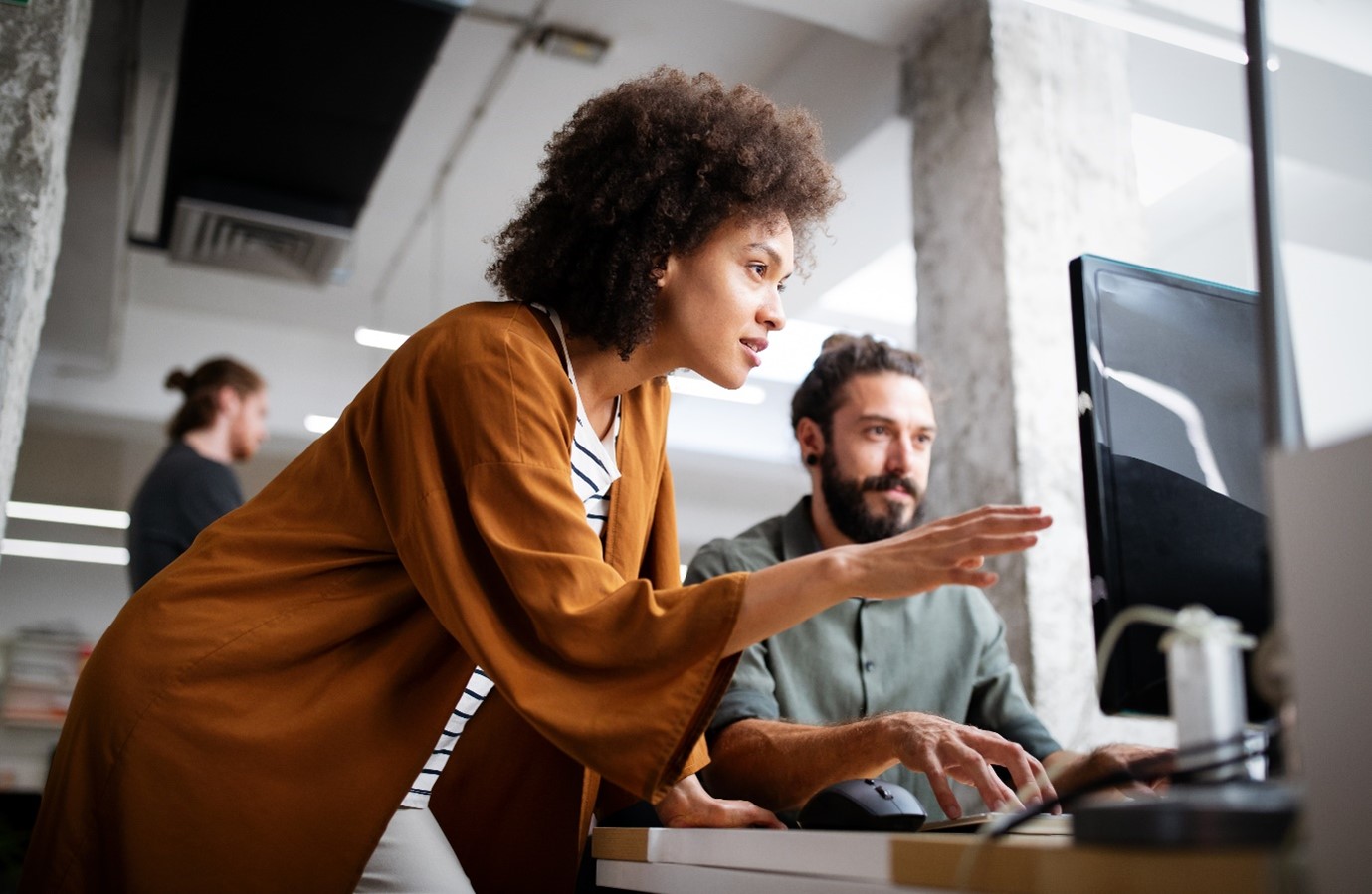 Two team members collaborating at a computer in a modern office, illustrating the theme What working with clients taught me about UX communication.